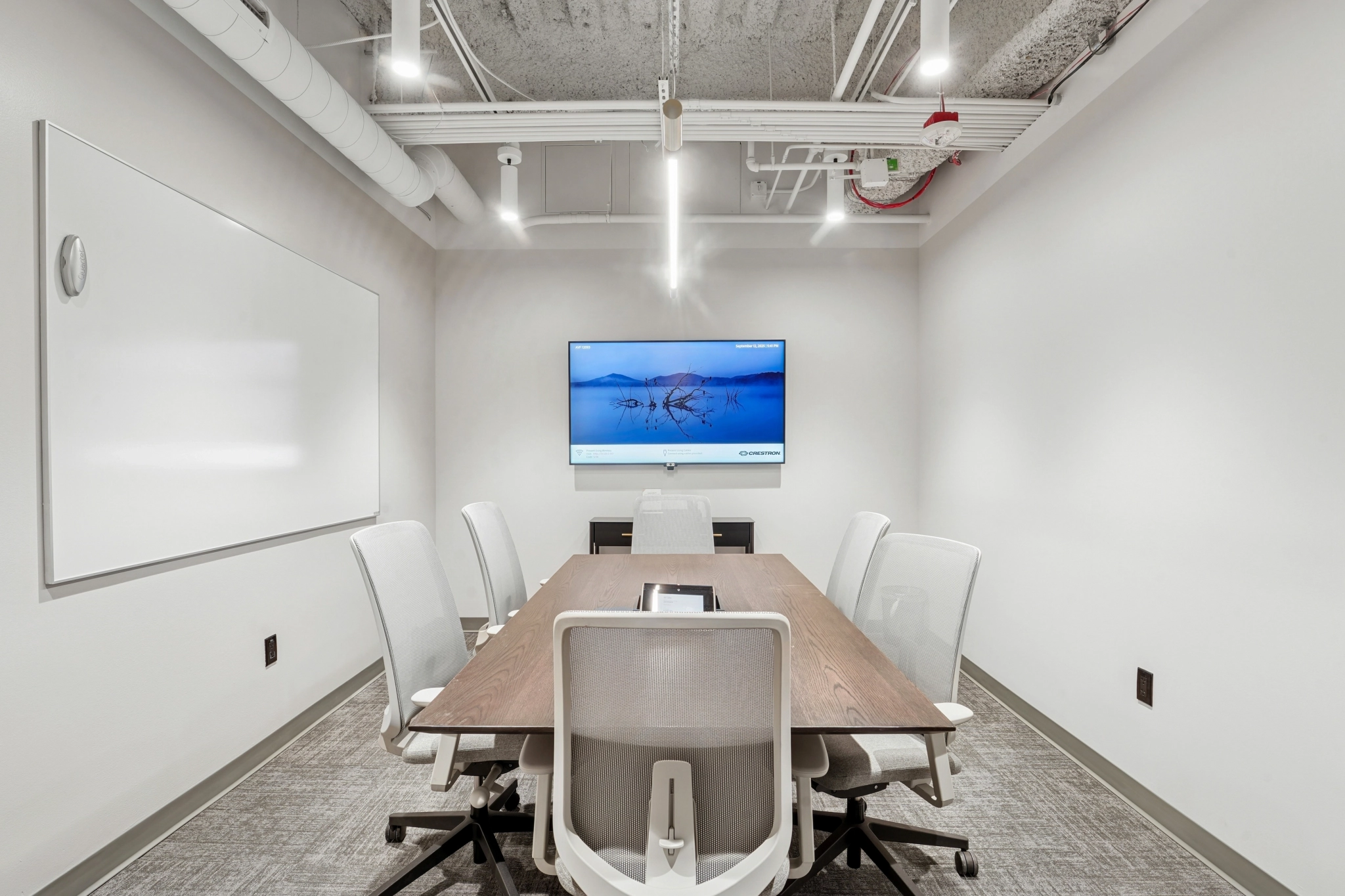 Esta acogedora sala de reuniones de Seattle cuenta con seis sillas blancas en una mesa de madera, una pantalla de pared con un cuadro y una pizarra blanca: ideal para sesiones de trabajo productivas.