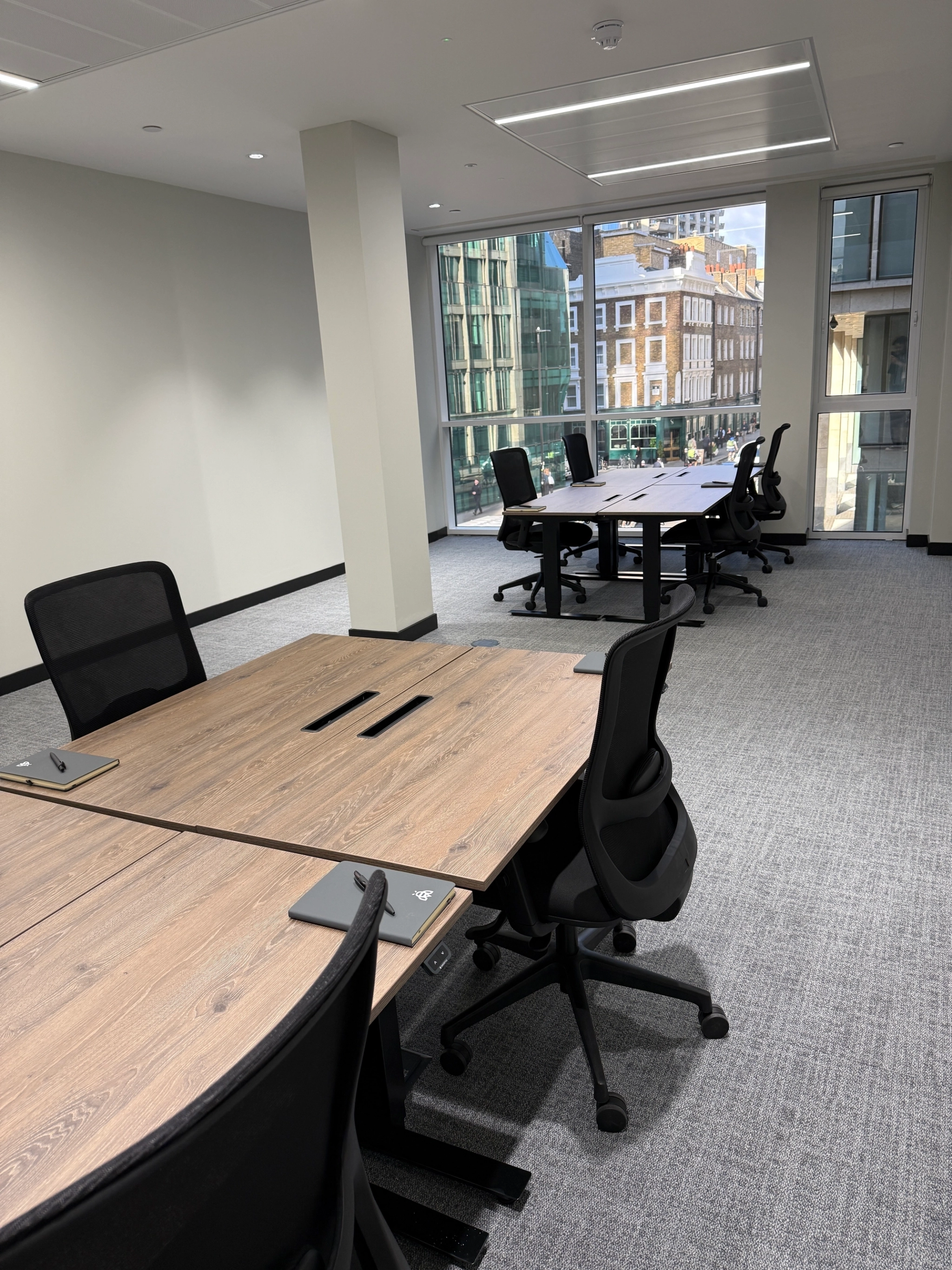 A modern London office with desks and chairs, large windows, and a view of city buildings outside.