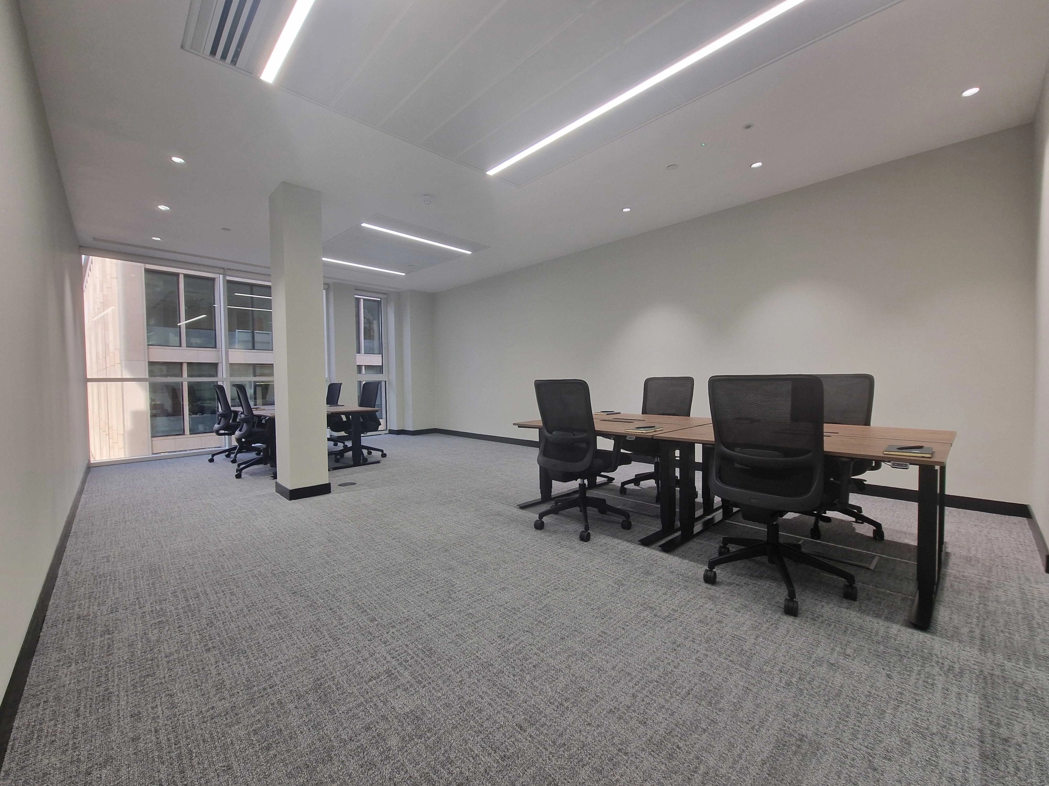 Spacious London workspace with desks, several black office chairs, a carpeted floor, and large windows letting in natural light.