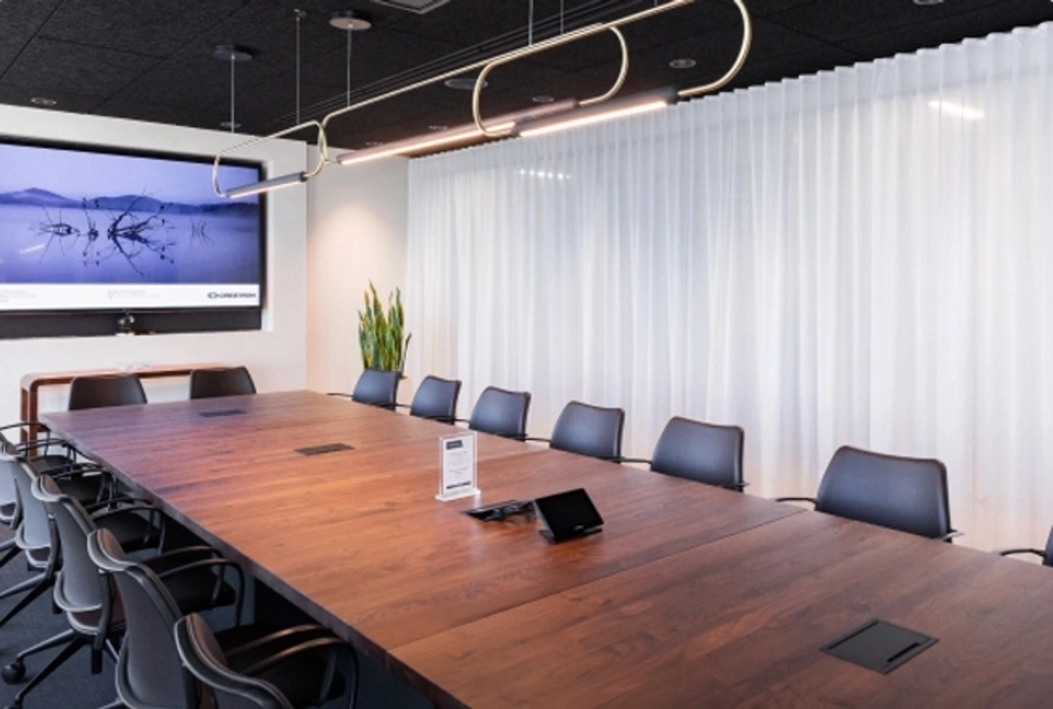 A modern East Palo Alto conference room with a long table, twelve chairs, a wall-mounted TV displaying the Zoom app, a whiteboard, and a tablet on the table—perfect for coworking or team meetings.
