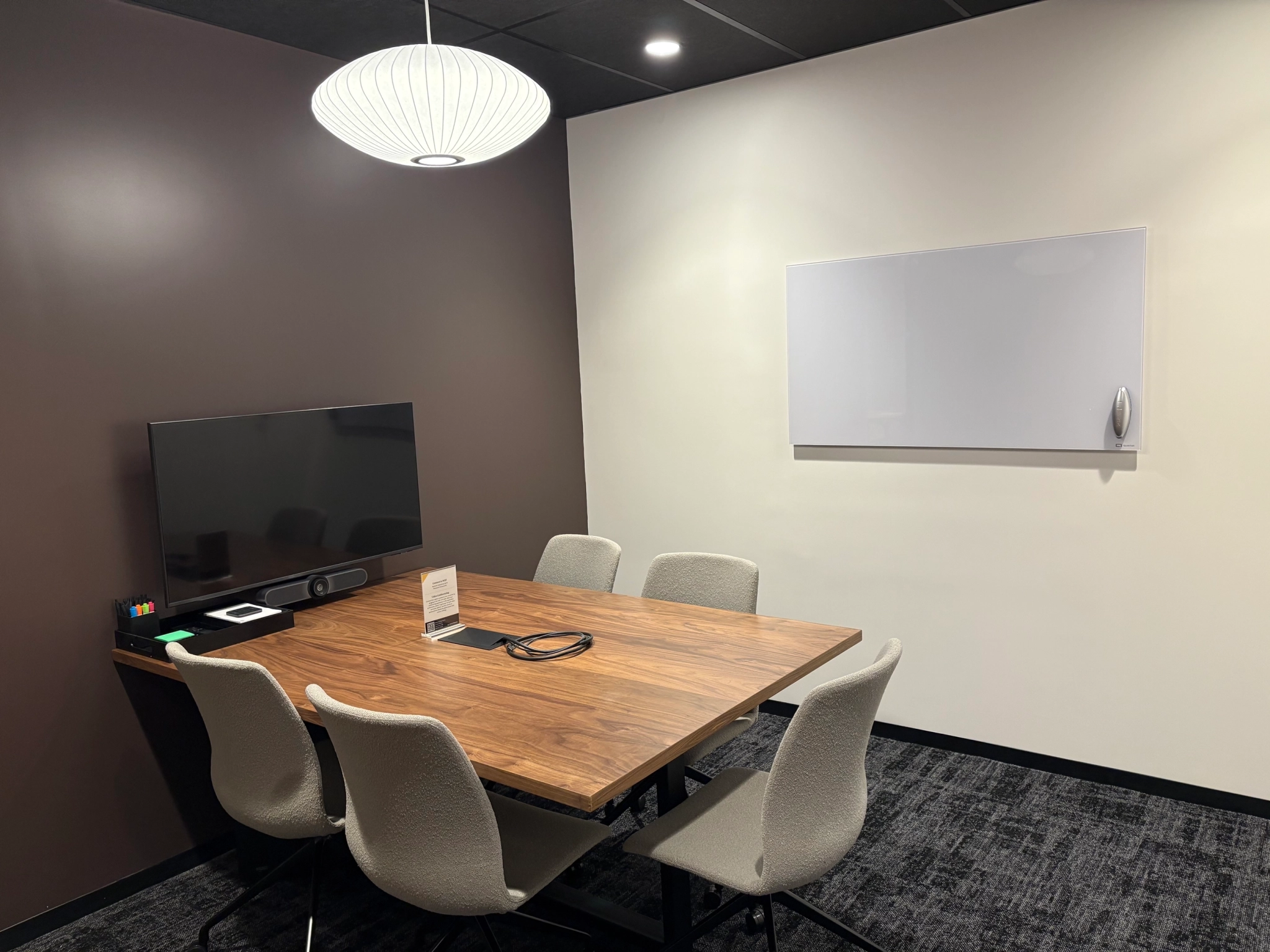 A modern meeting room in New York with a wooden table, six chairs, a wall-mounted TV, a whiteboard, and a ceiling light—perfect for a productive workspace.